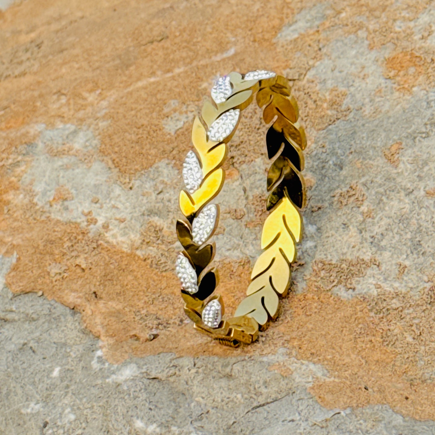 Gold and silver leaf-patterned bracelet on a stone surface