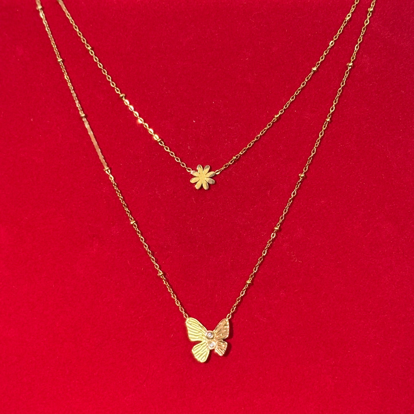 Two gold necklaces with floral and butterfly pendants on a red surface.
