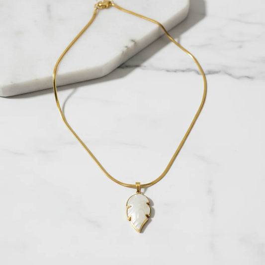 Gold necklace with a white pendant on a marble surface