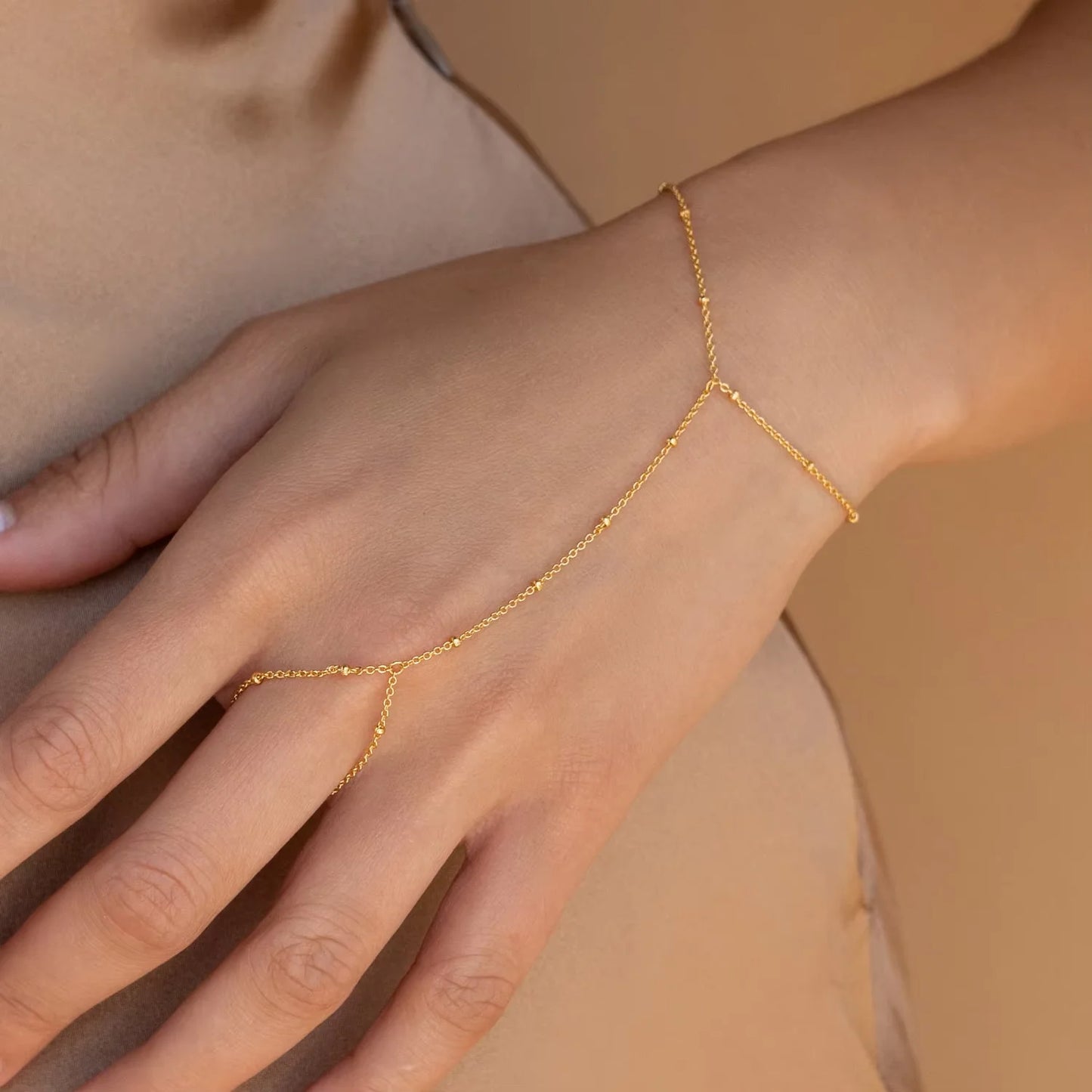 Gold bracelet on a person's wrist against a beige background