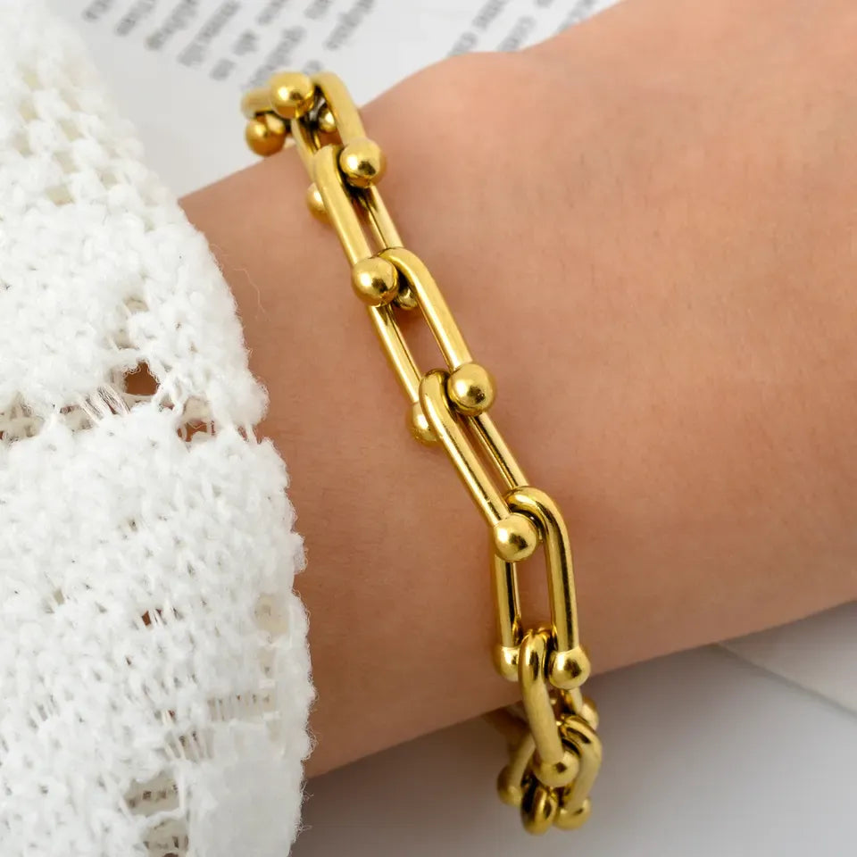 Gold chain bracelet on a wrist with a white lace garment in the background