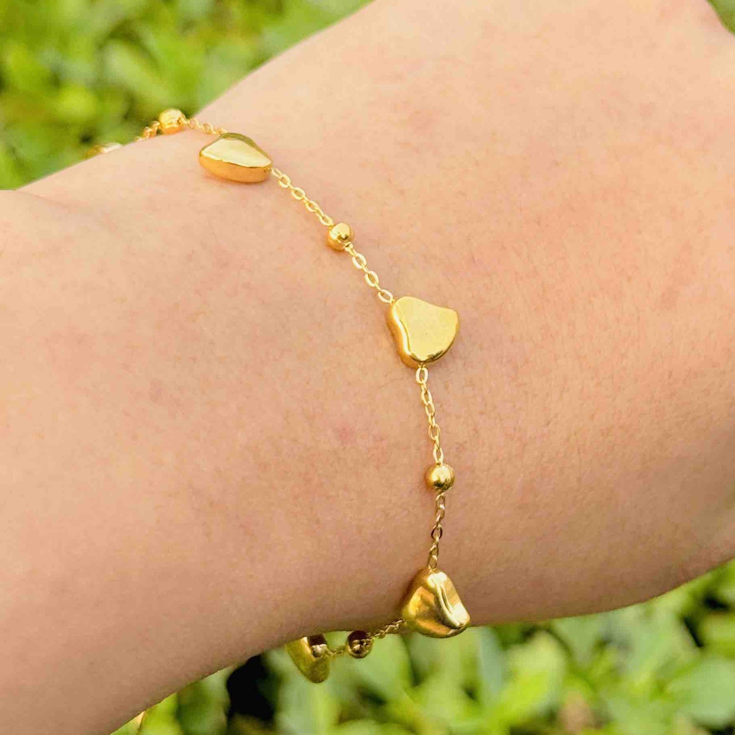 Gold bracelet with heart-shaped charms on a wrist against a blurred green background