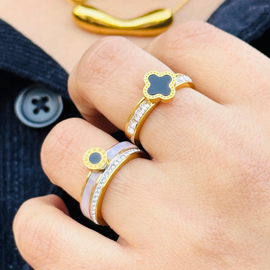 Close-up of a hand wearing two gold rings with blue stones on a dark fabric background.