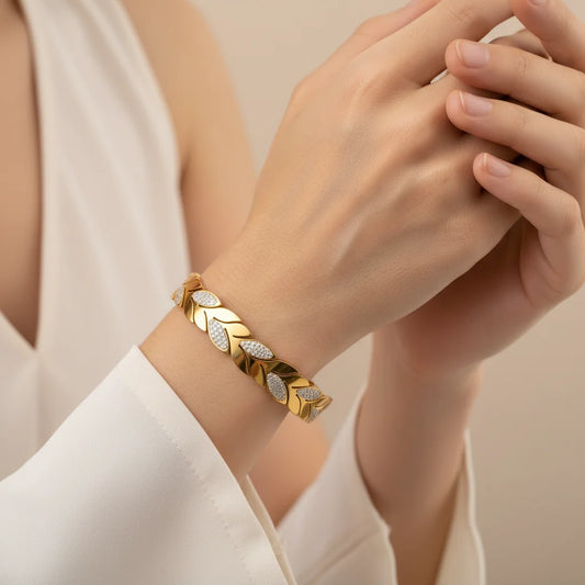 Gold bracelet with leaf design on a person's wrist against a neutral background