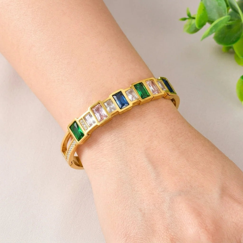 Gold bracelet with multicolored gemstones on a wrist against a neutral background