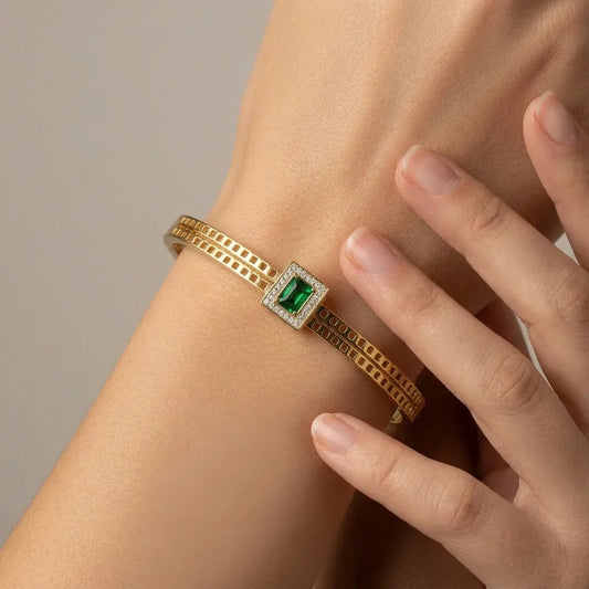 Gold bracelet with a green gemstone on a wrist against a neutral background