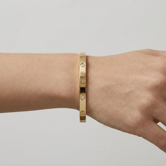 Gold bracelet on a wrist against a neutral background