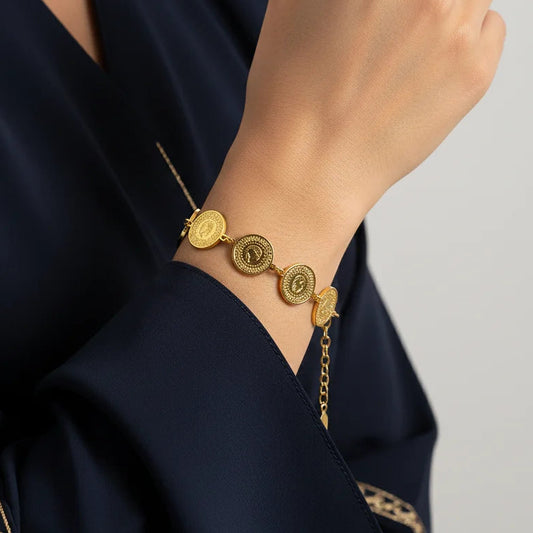 Gold bracelet on a person wearing a dark blue garment with gold embroidery.