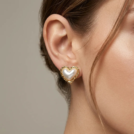 Heart-shaped earring with pearl center worn by a person against a neutral background
