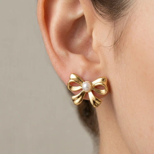 Gold bow-shaped earring with a pearl center worn by a person.