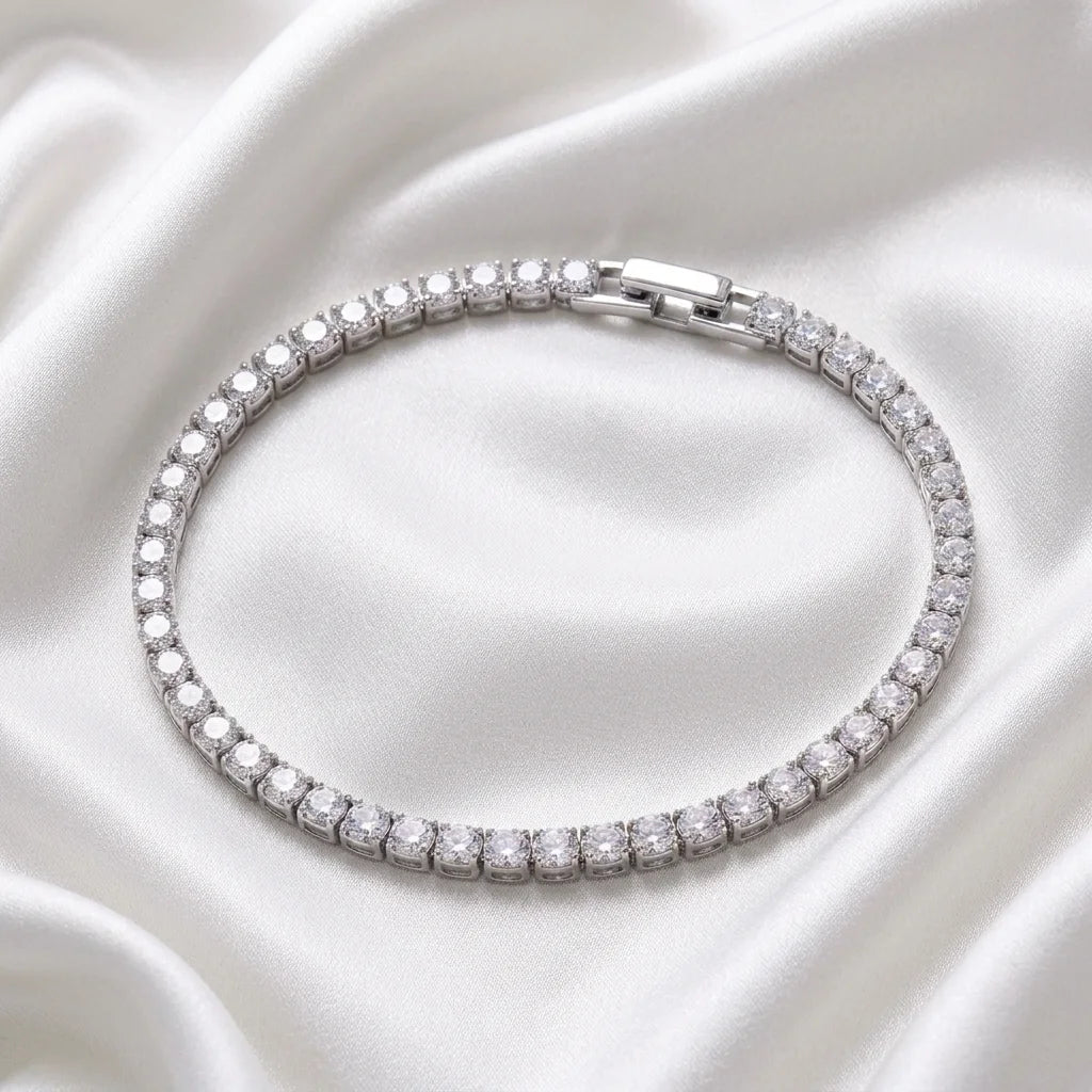 A silver tennis bracelet encrusted with clear cubic zirconia stones, arranged in a neat circle on a draped white satin fabric background.