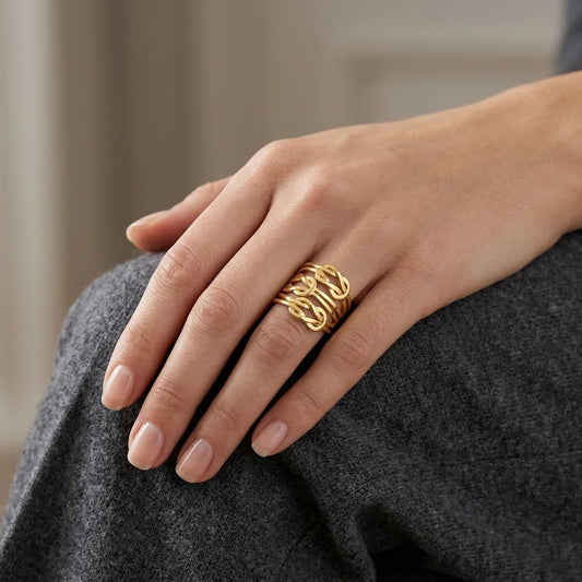 A close-up of a person's hand resting on gray fabric, wearing a gold ring with an intricate, interlocking chain-like design.