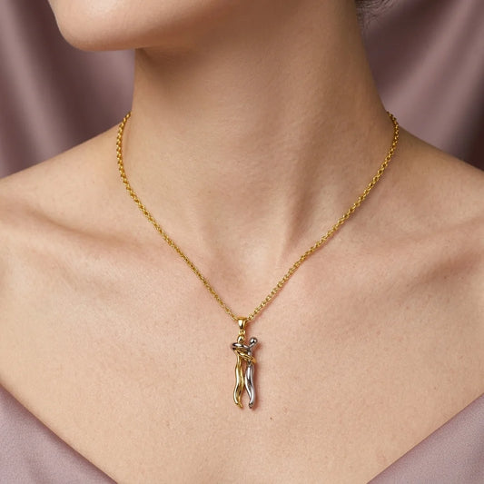 A close-up of a model's neck and chest wearing a delicate gold chain necklace with a small pendant shaped like a stylized female figure in gold and silver.