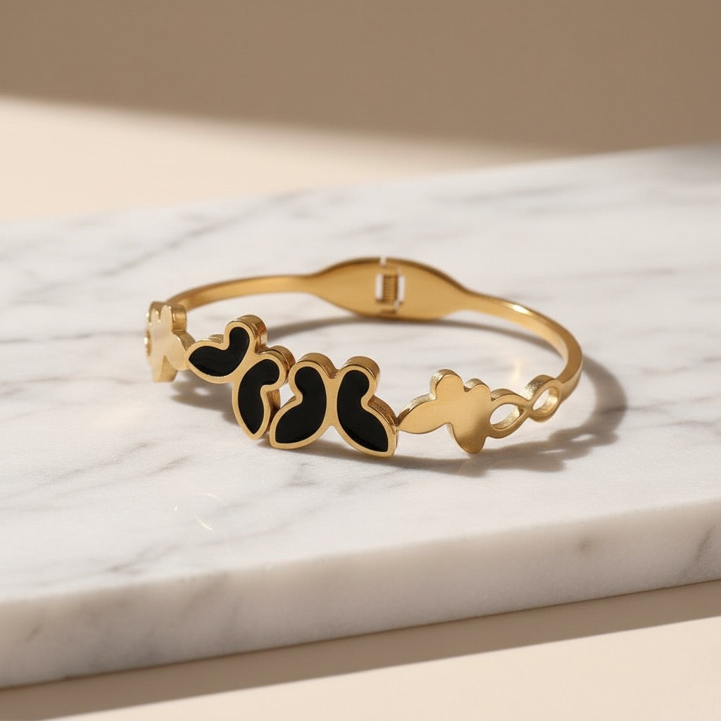 Gold bracelet with black heart-shaped stones on a marble surface