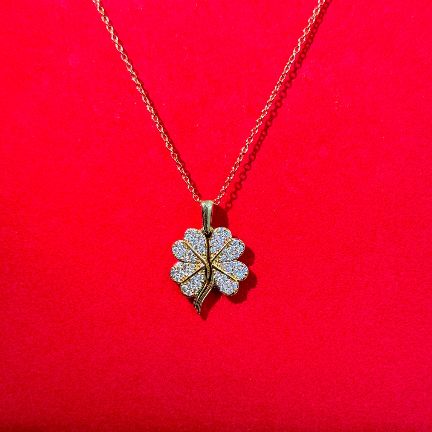 Gold necklace with a four-leaf clover pendant on a red background