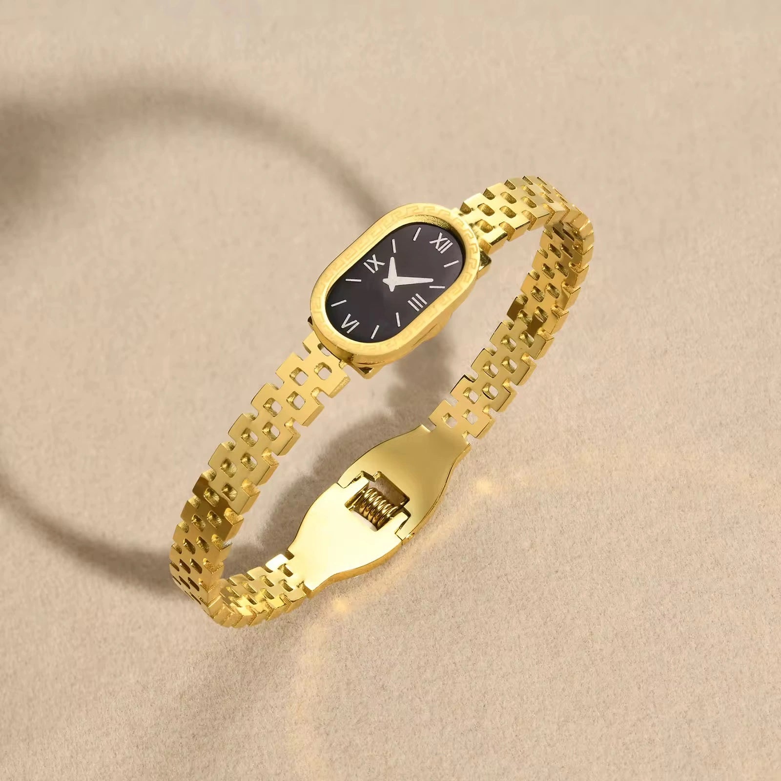 Gold bracelet with a black watch face on a beige background