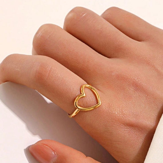 Gold heart-shaped ring on a person's finger against a neutral background