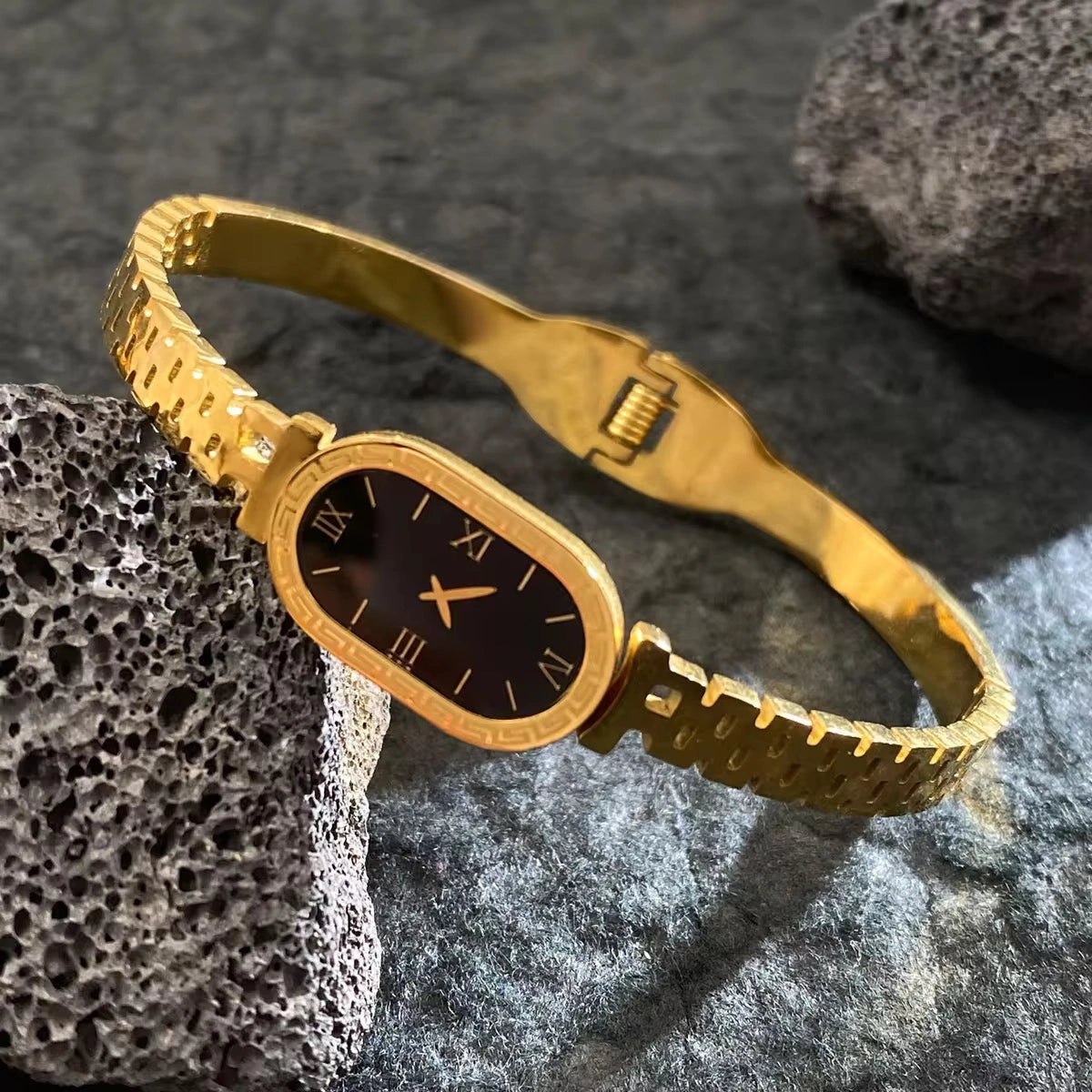 Gold bracelet with a black face on a textured stone surface