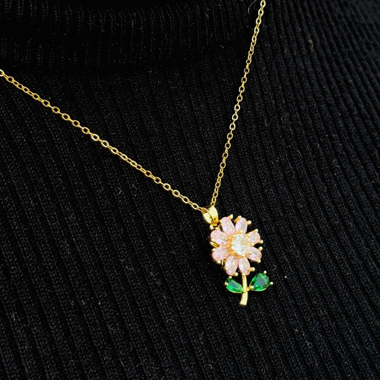 Gold necklace with a pink flower pendant on a black background