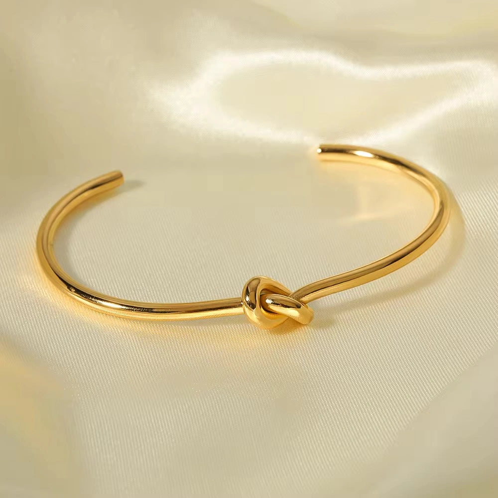 Gold bracelet with a knot design on a beige fabric background