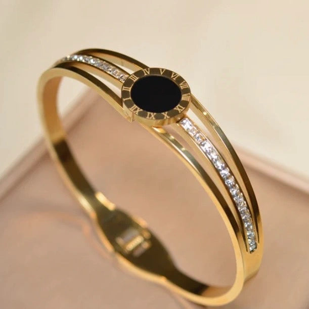 Gold bracelet with a black center and diamonds on a beige background