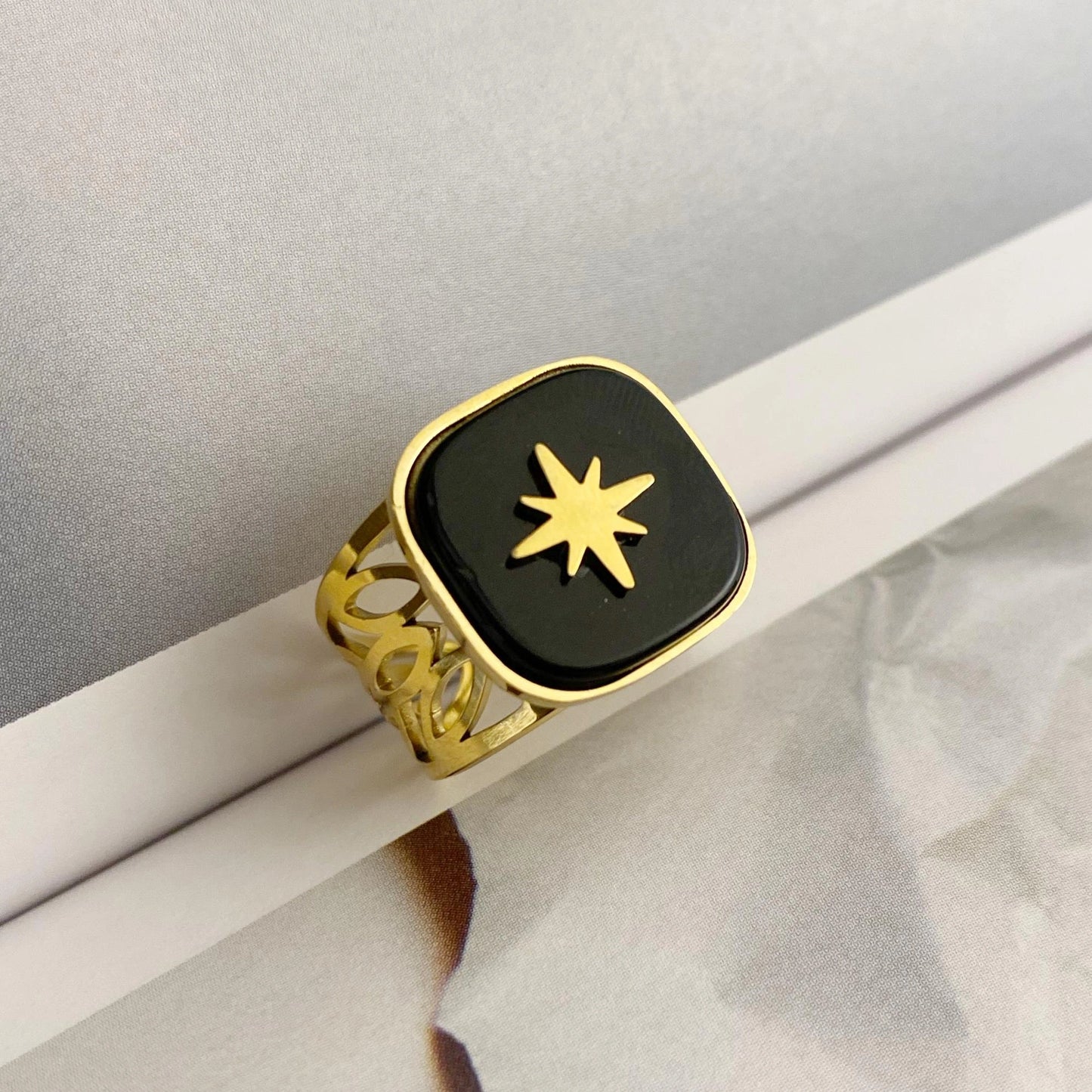 Gold ring with a black square face and star design on a white surface.