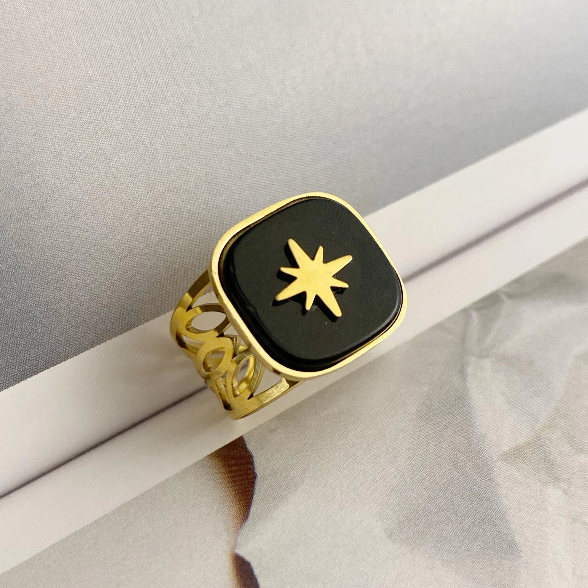 Gold ring with a black square face and star design on a white surface.