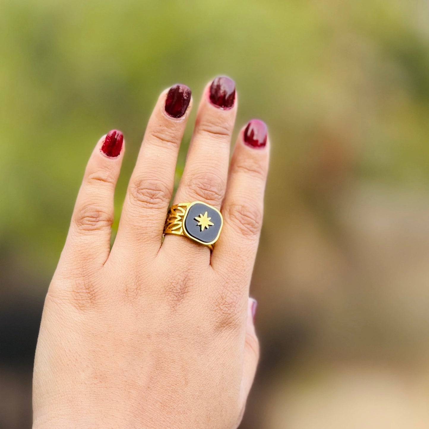 Hand wearing a gold ring with a blue stone against a blurred green background