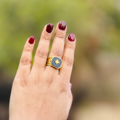 Hand wearing a gold ring with a blue stone against a blurred green background
