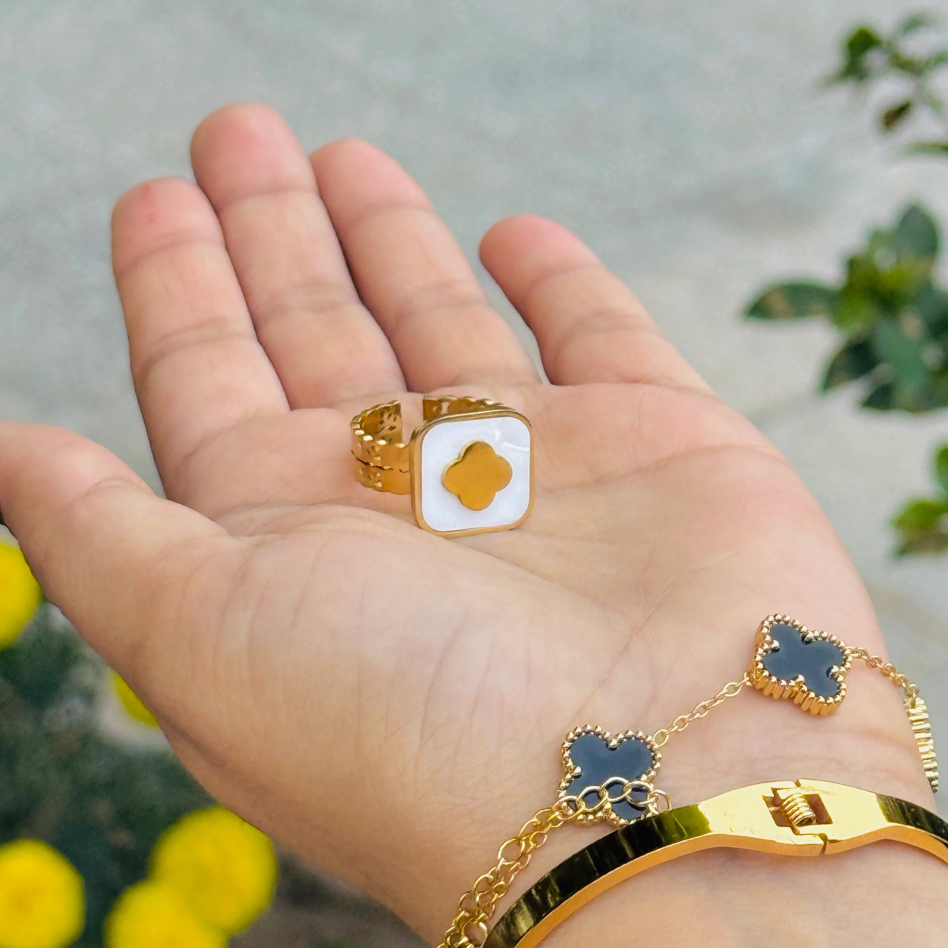 Gold ring with a white center on a hand, with a blurred background of greenery.