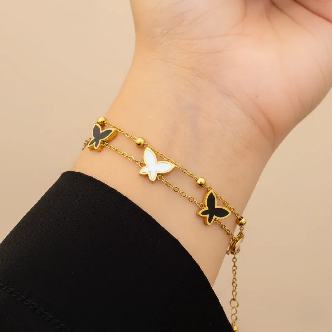 Gold bracelet with butterfly charms on a wrist against a beige background