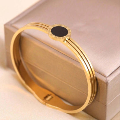 Gold bracelet with a black center stone on a beige box
