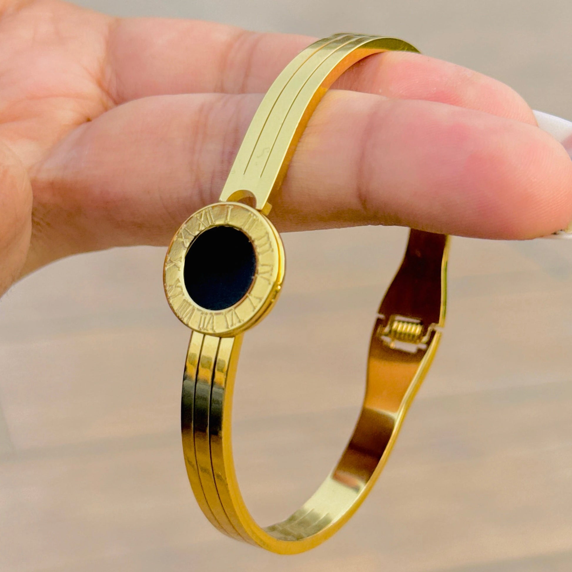 Gold bracelet with a black stone held by a hand against a neutral background