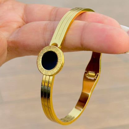 Gold bracelet with a black stone held by a hand against a neutral background