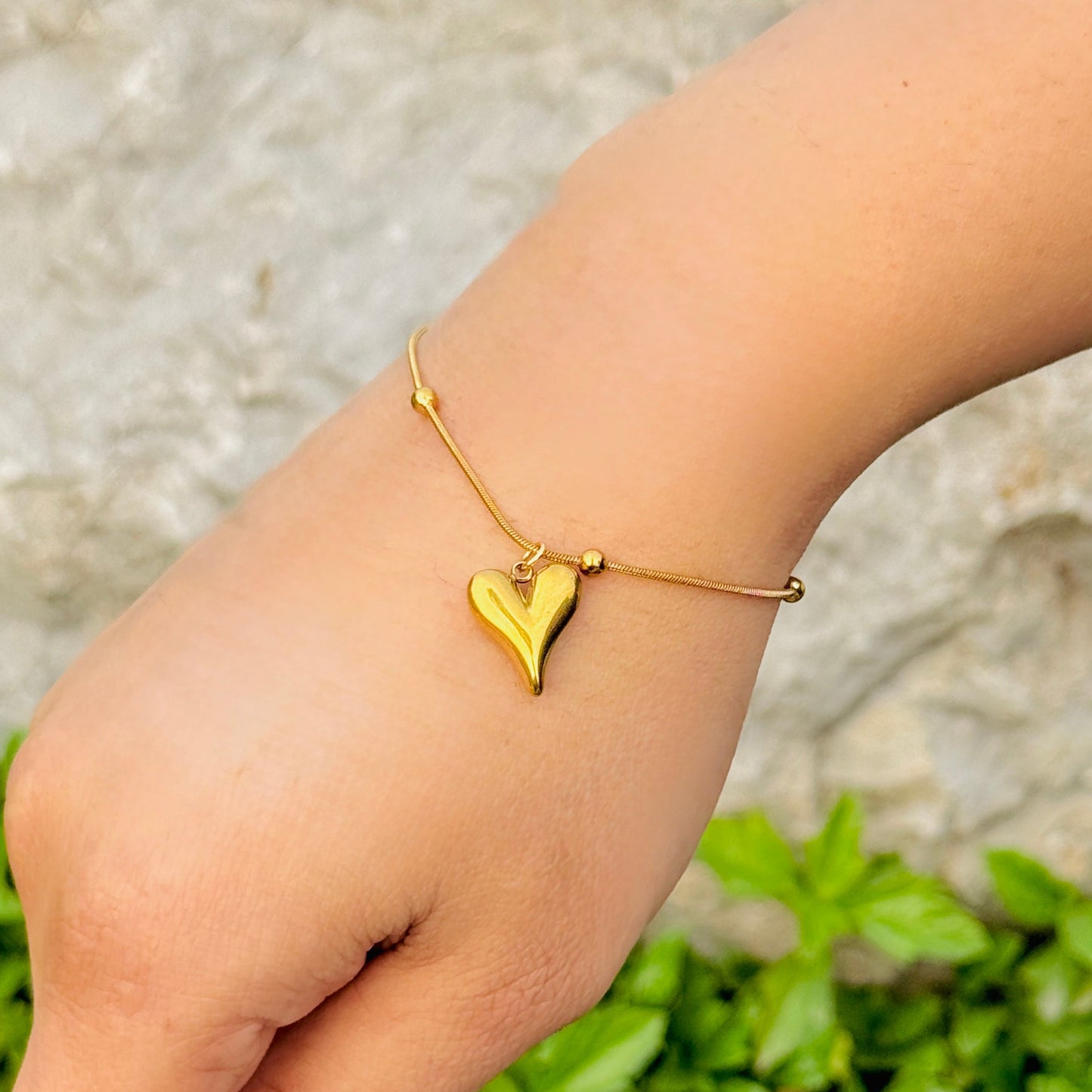 Gold heart-shaped bracelet on a wrist with a blurred natural background