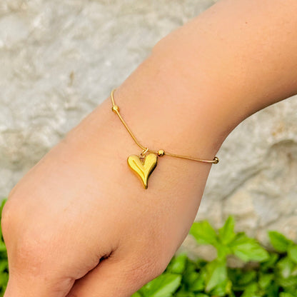 Gold heart-shaped bracelet on a wrist with a blurred natural background