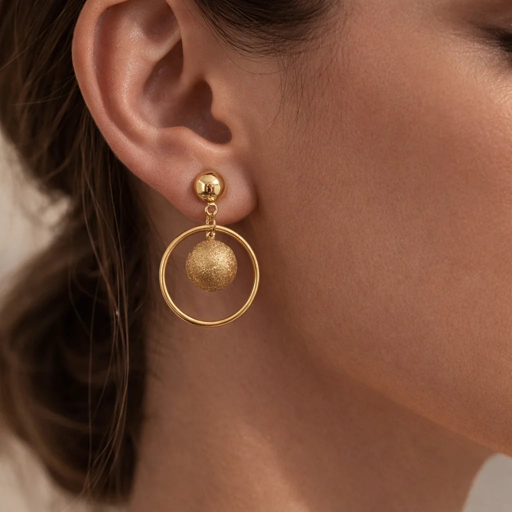 Gold hoop earrings with embedded spherical charms worn by a person.