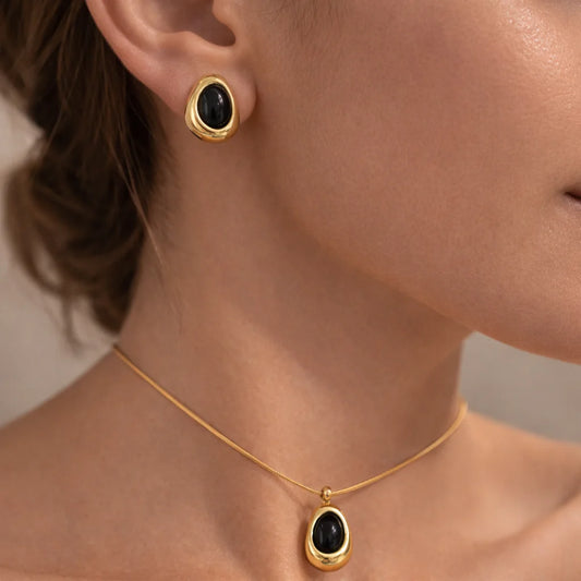 Gold necklace and earrings with black stones worn by a person