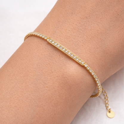 Gold bracelet with small diamonds on a wrist against a light background