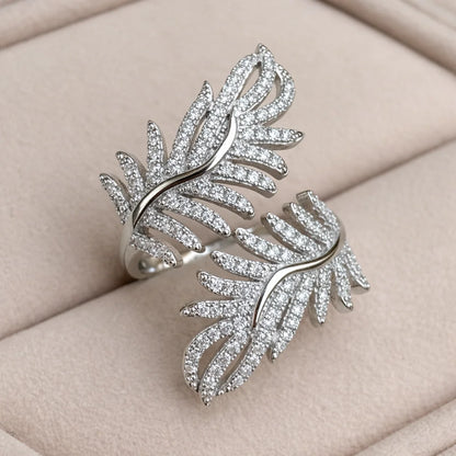 Silver feather-shaped ring with gemstones on a beige cushion