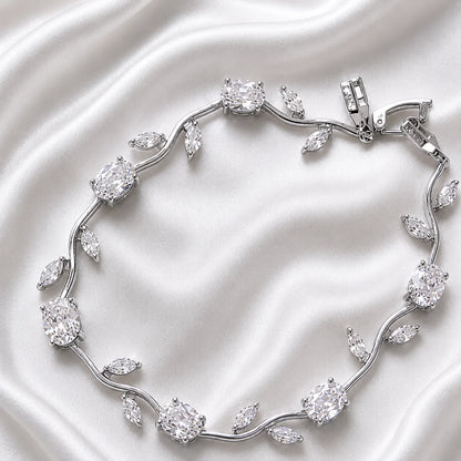 A silver-toned vine bracelet with clear gemstones arranged in leaf and oval motifs, photographed on a draped white satin fabric background.