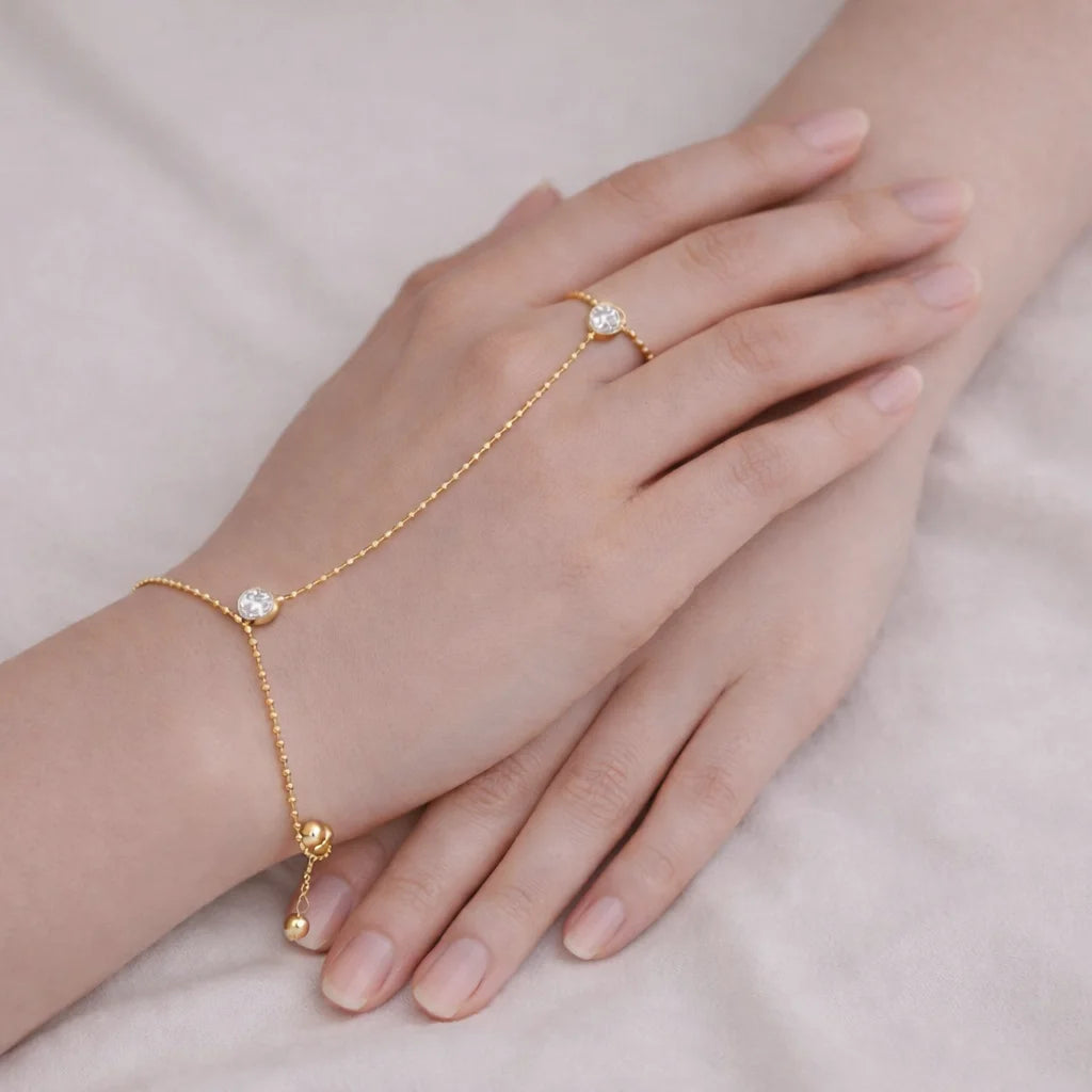 Gold bracelet and ring on a hand against a neutral background