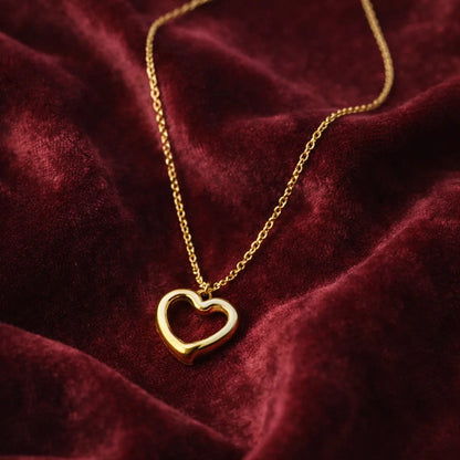 Gold heart-shaped pendant necklace on a burgundy fabric background