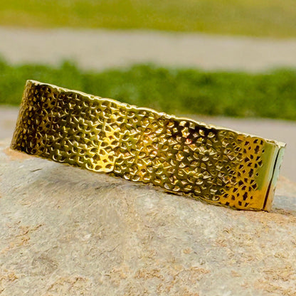 Gold textured bracelet on a rock with grass in the background