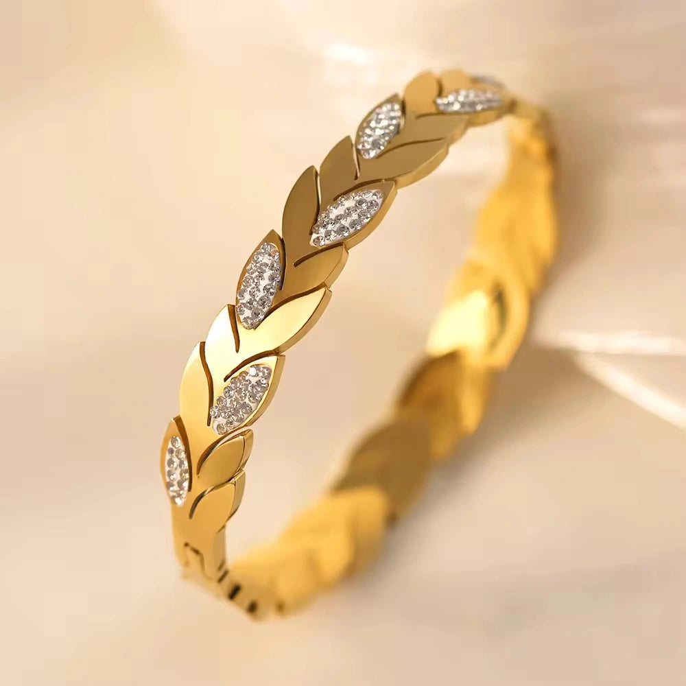 Gold bracelet with leaf design and embedded stones on a beige background