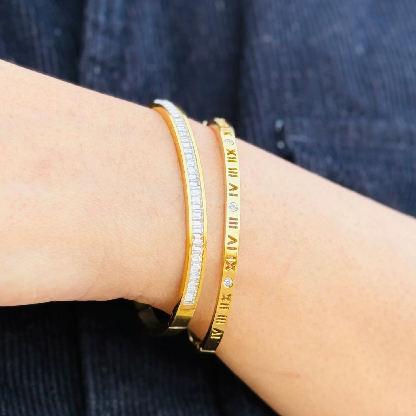 Gold bracelet with embedded stones on a wrist against a dark fabric background