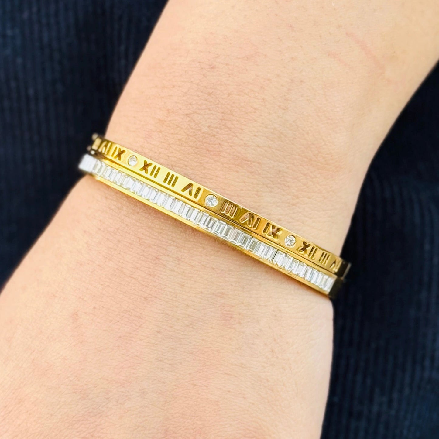 Gold bracelet with Roman numeral design on a wrist against a dark background