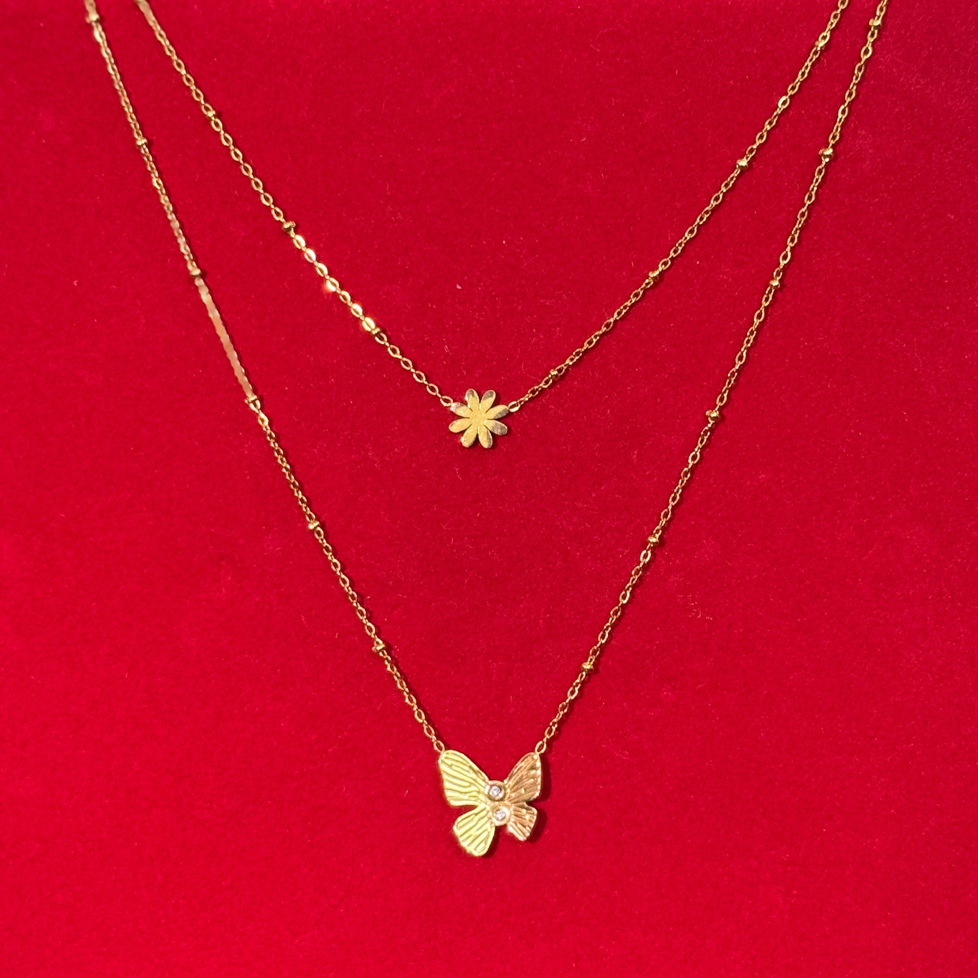 Two gold necklaces with floral and butterfly pendants on a red surface.