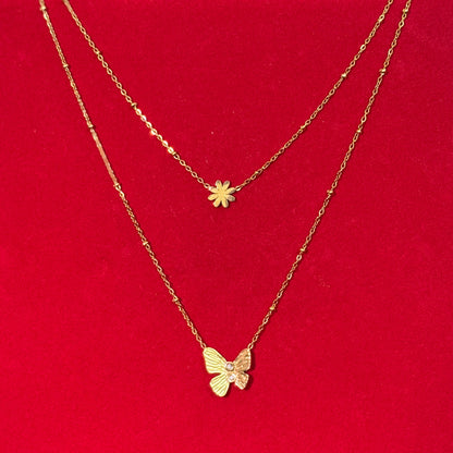 Two gold necklaces with floral and butterfly pendants on a red surface.