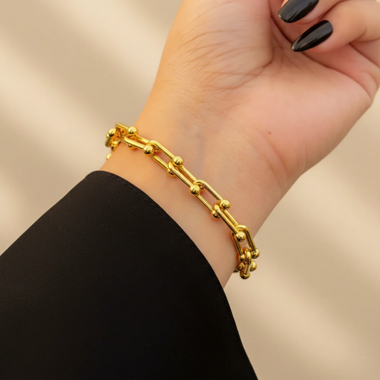 Gold chain bracelet on a wrist with a neutral background